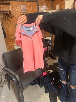 Rosa henley från Happy Camper - Säljer en rosa henley från Happy Camper med korta ärmar och ljusblå insida vid kragen. Skjortan har en klassisk krage och knappar framtill. Perfekt för dig som gillar en avslappnad och enkel stil.