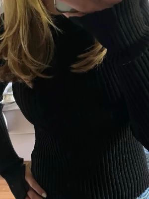 Svart ribbad stickad tröja-glittrig - Säljer en svart ribbad stickad tröja med lång ärm och figurnära passform. Perfekt till jeans eller kjol för en clean och enkel look. Tröjan har hög hals och är supermjuk och skön att bära.