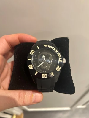 Zadig & Voltaire svart klocka Rock'n Roll Skull - Cool svart klocka från Zadig & Voltaire med texten 'ROCK'N ROLL' på urtavlan och en graverad döskalle. Armbandet är i svart syntetmaterial och spännet har ZV-logga. Kommer i original ask. Perfekt accessoar för dig som gillar edgy stil. Batteri behöver bytas. Oanvänd. 