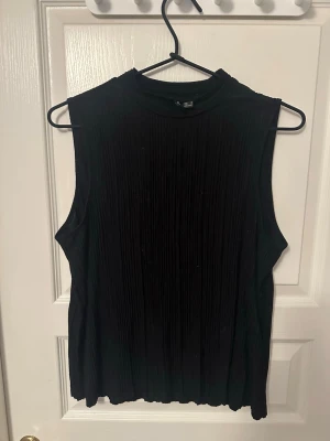 Ribbad topp  - Säljer en svart ärmlös topp från Vero Moda i storlek S. Toppen har en hög hals och är ribbad med fina vertikala veck som ger ett snyggt fall. Perfekt att styla med jeans eller kjol för en clean look.💋😽