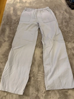 Ljusblå linnebyxor från H&M - Säljer ett par ljusblå linnebyxor från H&M med resår i midjan och stora fickor framtill. Byxorna har en relaxed passform och raka ben, perfekta för chill dagar. Materialet är svalt och skönt, och färgen är riktigt fräsch till sommaren.