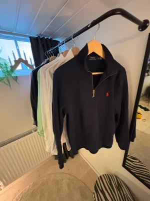Marinblå half zip från Polo Ralph Lauren - Säljer en marinblå långärmad tröja från Polo Ralph Lauren med klassisk röd logga på bröstet. Tröjan har en snygg half zip-dragkedja och hög krage. Tillverkad i mjuk bomull som är skön att bära. Perfekt till jeans för en stilren look.