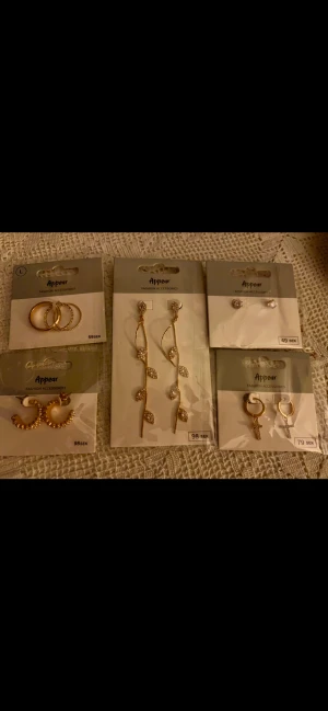 Guldfärgade smycken med strass från Åhléns  - Nickel fria, 4par örhängen och 1par ringar. Från Åhléns liten platspåse till varje ingår ( är som skydd för dem ) Helt nya aldrig använda 