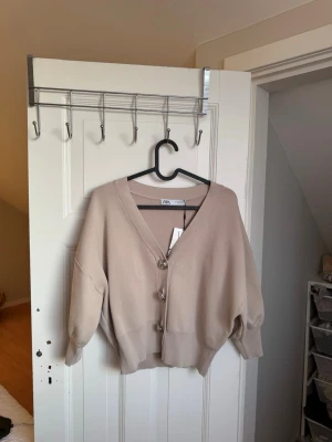 Beige kofta från Zara med coola knappar - Säljer en beige kofta från Zara med unika silvriga knappar framtill. Ny med prislapp! 