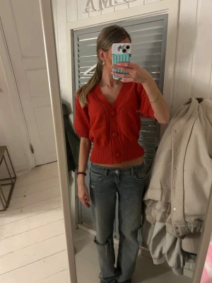 Röd kofta från Freequent, kort ärm - Säljer en röd kofta från Freequent i storlek XS. Koftan har korta puffärmar, djup v-ringning och stora matchande knappar framtill. Den är ribbstickad i nederkant och vid ärmslut, vilket ger en snygg och modern look.