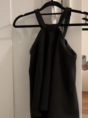 Svart halterneck topp - Säljer en svart halterneck topp med breda axelband. Toppen har en lös passform och är ärmlös. Toppen är från hm i storlek 36. 