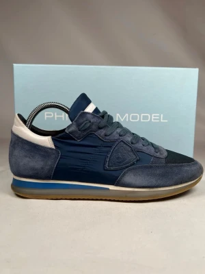 Blå sneakers från Philippe Model - Snygga sneakers från Philippe Model i olika blå nyanser med detaljer i vitt. Ovandelen är i mocka och textil, med mesh framtill och klassisk snörning. Sidan pryds av märkets logotyp och sulan har en blå rand för extra stilpoäng. Orginalbox ingår.