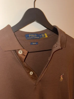 Brun henley från Polo Ralph Lauren - Brun långärmad piké från Polo Ralph Lauren i slim fit. Storleken är S/M, passar längden 175-180