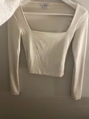 Vit långärmad topp från Amisu XS - Säljer en stilren vit topp från Amisu i storlek XS. Toppen har lång ärm och en fyrkantig urringning som ger en modern vibe. Materialet är mjukt och stretchigt, perfekt för att matcha med jeans eller kjol. Liten fläck men syns knappt