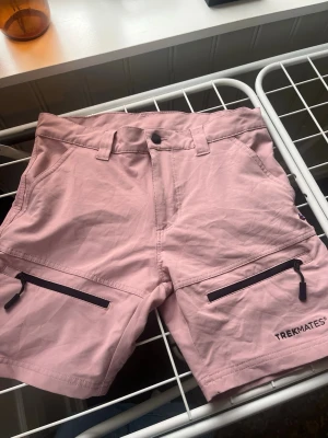 Rosa shorts från Trekmates  - Säljer ett par ljusrosa frilufts shorts från Trekmates i storlek XS. De har två svarta dragkedjefickor framtill, bälteshällor och knappstängning m dragkedja. Materialet känns lätt och smidigt, perfekt för sommardagar. Snygg och enkel design som funkar till det mesta. Nästan aldrig använda!