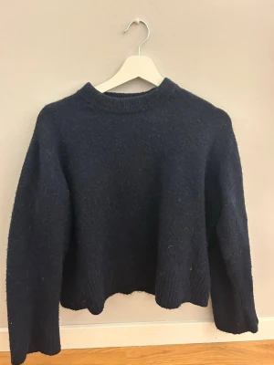 Mörkblå stickad tröja - Mysig mörkblå stickad tröja med rund hals och långa ärmar. Tröjan har en enkel, klassisk design med ribbade muddar vid ärmslut och nederkant. Perfekt för kyliga dagar och enkel att matcha med olika outfits.