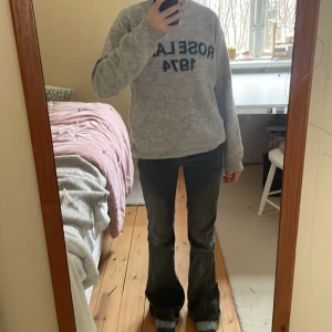 Grå stickad tröja HM - Mysig grå stickad tröja från H&M med texten ROSE LANE 1974 i svart framtill. Tröjan har rund halsringning, långa ärmar och ribbade muddar vid ärmslut och nederkant. Perfekt för kyliga dagar och enkel att matcha med jeans.