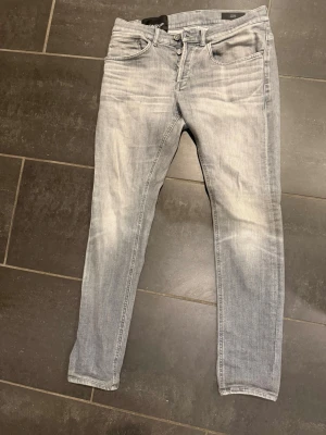 Ljusgrå skinny jeans från Dondup  - Säljer ett par ljusgrå skinny jeans från Dondup med klassisk femficksdesign och knappgylf. Jeansen har en snygg tvättad look och smal passform som sitter tajt längs benen. Perfekta för dig som gillar en clean och modern stil.