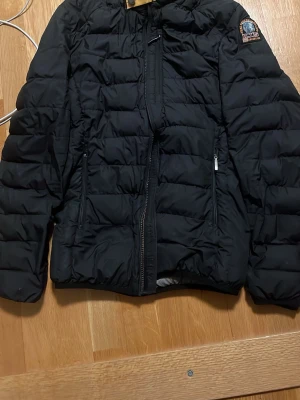 Svart pufferjacka från Parajumpers - Säljer en svart pufferjacka från Parajumpers med klassisk patch på ärmen. Jackan har quiltad design, dragkedja framtill och två sidofickor med dragkedja. Perfekt för kalla dagar och riktigt snygg till alla outfits.