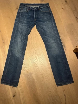 Levi's 501 blå jeans W31 L34 - Klassiska blå Levi's 501 jeans med rak passform och knappgylf. Jeansen har fem fickor, tydliga kontrastsömmar och den ikoniska läderpatchen bak i midjan. Tillverkade i slitstarkt bomullsjeansmaterial. Perfekta för dig som gillar tidlös denimstil. Står 33/34 på lappen men passar som en 31 eller 32 midjan, kan skicka måtten om man undrar.