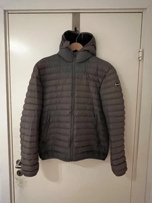 Collar jacka - Säljer en grå pufferjacka från Colmar med huva och dragkedja framtill.  Perfekt för kyliga dagar och riktigt snygg. Storlek 48, motsvarar M.  Skick: 9/10, den har inga defekter. 