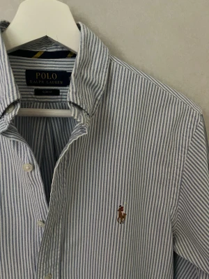 Ralph Lauren Skjorta - Riktigt stilig Ralph Lauren skjorta i dunder skick och randig med vit/ljusblå färg. Skjortan är i storlek S och den mest eftertraktade modellen Slim Fit. Vid frågor eller funderingar tveka inte på att höra av er! 😊