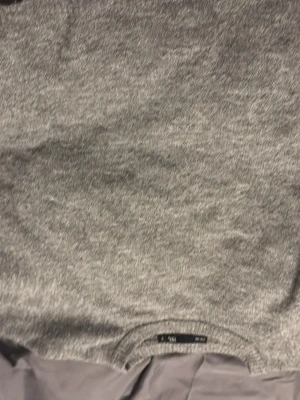 Grå stickad tröja från 157 - Mysig grå stickad tröja från 157 med rund halsringning och ribbade muddar. Perfekt för  kyliga dagar. Enkel och stilren design som passar till allt. Lite stor i storleken eftersom den är lös