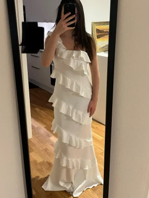 Vit långklänning med volanger oneshoulder - Supersnygg vit långklänning med volanger i flera lager och oneshoulder-design. Klänningen har en elegant och flowy känsla, perfekt för dig som vill sticka ut. Materialet känns lätt och svalt, och volangerna ger en extra touch av stil. Helt oanvänd utan prislapp!!🤩