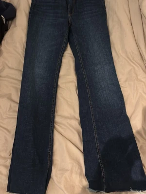 Mörkblå raka jeans med rå kant , högmidjade  - Säljer ett par mörkblå jeans med rak passform och rå, fransig kant längst ner på benen. Jeansen har klassisk femficksdesign och kontrastsömmar. Perfekta för dig som gillar en avslappnad och trendig look.