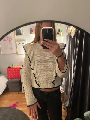 Vit stickad volangtröja H&M Divided XS - Superfin vit stickad tröja från H&M Divided i storlek XS. Tröjan har volangdetaljer framtill och längs axlarna med svarta kanter som ger en snygg kontrast. Långärmad och croppad modell, perfekt till jeans eller kjol.