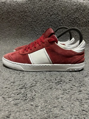 Valentino flycrews - Snygga sneakers från Valentino Garavani i rött och vitt med platt sula och rund tå. Ovandelen är i mocka och skinn, med röda snören och vita detaljer på sidorna och hälen. Ikoniska nitar på sulan ger extra edge till looken.