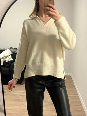 Beige stickad polotröja med krage - Säljer en beige stickad polotröja med v-ringning och krage. Tröjan har lång ärm, ribbade muddar och slits i sidorna. Oversized och chill passform, perfekt till skinnbyxor eller jeans.