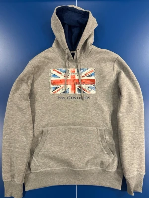 Pepe Jeans hoodie - En riktigt fet grå Pepe Jeans hoodie med flaggan av Storbritannien. Hoodien är i storlek Small men är lite lösare så passar också Medium. Skicket är 8/10 hoodien är väldigt sparsamt använd och har mest legat i garderoben, smått tecken på använd kan förekomma. Kom dm för fler frågor osv!