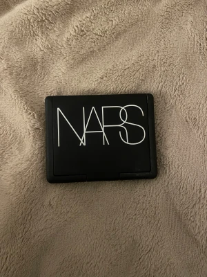 NARS Rouge Torrid Persikofärgad - Rouge från NARS i nyansen Torrid, en persikofärgad ton med lätt skimmer. Kommer i en stilren svart dosa med spegel i locket, perfekt att ha med i väskan. Ger kinderna en fräsch och naturlig glow.
