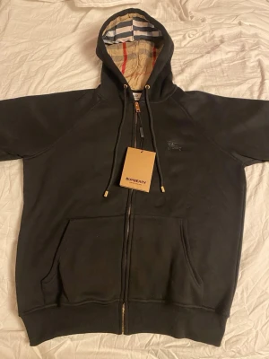 Svart burberry zip up hoodie - Svart zip up hoodie från burberry i storlek M med rutigt foder i huvan och broderad logga på bröstet. Pris kan diskuteras vid snabbt köp. Skriv om ni har några frågor.