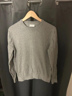 Grå stickad tröja från Grunt XL - Snygg grå stickad tröja från Grunt i storlek XL för barn. Tröjan har rund halsringning och ribbade muddar vid halsen. Perfekt för dig som gillar enkel och stilren design. Materialet är mjukt och skönt, passar till många olika outfits.