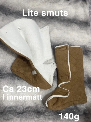 Bruna quiltade tofflor 23cm - Mysiga bruna quiltade tofflor med vit fleecefodring. Perfekta att dra på sig hemma för extra värme. Stängs med kardborreband och har en mjuk, platt sula. Lätta och sköna, väger endast 140g. 🌸 Fint använt skick. Står ingen storlek men är 23cm i innermått kollade upp i en storleksguide att det motsvarade storlek 37 men följ innermåttet som är angivet istället. Lite smuts.