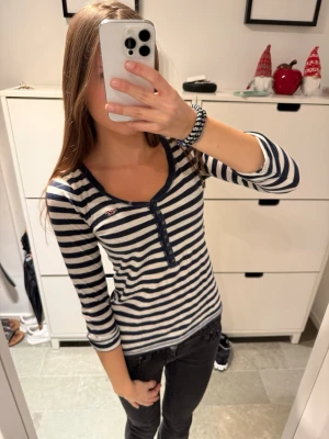 Hollister unik randig henley topp  - Topp från Hollister i marinblått och vitt med klassiska ränder. Toppen har u-ringning, knappar framtill, uppvikta armar och ett litet broderat Hollister-logo på bröstet.