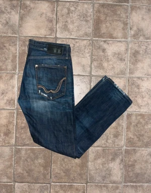 Replay jeans  - Snygga mörkblå jeans från Replay med klassisk straight fit och coola slitningar. Bakfickorna har kontrastsömmar och Replay-logga. Jeansen är tillverkade i slitstarkt bomullsjeansmaterial och har normal passform. Midja 43cm, längd 108cm. JAG SKICKAR EJ FLER BILDER NÄR JAG BÄR JEANSEN! för storleksguide hänvisar jag till måtten och för bättre inblick i passformen rekommenderar jag att googla på modellnamnet. Jeansen kan vara uppsydda utan att jag noterat det så kolla måtten noggrant :) s4