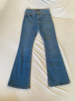 Blå bootcut jeans från TEY - Snygga blå jeans från TEY i klassisk bootcut-modell. Jeansen har fem fickor, bälteshällor och stängs med knapp och dragkedja. Materialet är jeans med en skön känsla och passformen är normal. Perfekta för dig som gillar retrovibbar och utsvängda ben.