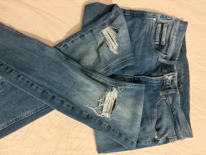 Blå Calvin Klein jeans med slitningar - Snygga blå jeans från Calvin Klein med slitna detaljer på båda benen. Modellen har klassisk femficksdesign, raka ben och normal passform. Jeansen är tillverkade i bomull med en skön stretch och har Calvin Klein-logga på knappen och insidan av linningen.