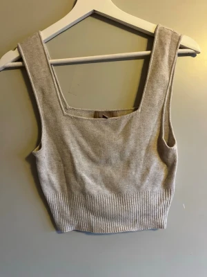 Beige stickad linnetopp från H&M - Säljer en beige stickad linnetopp från H&M i storlek S. Toppen har breda axelband, fyrkantig halsringning och ribbad nederkant som ger en snygg och chill look. Perfekt att styla med jeans eller kjol för en enkel vibe.