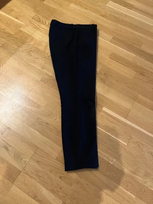 Svarta kostymbyxor/slacks med smal passform - Snygga svarta kostymbyxor/slacks med klassisk rak siluett och bälteshällor i midjan. Perfekta för en clean och stilren look. Materialet känns mjukt och följsamt, vilket gör dem bekväma att bära hela dagen.