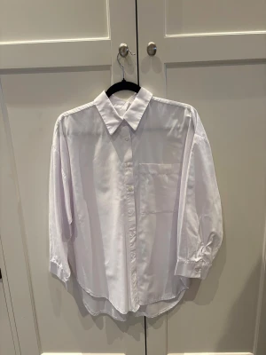 Vit klassisk skjorta med ficka och knappdetalj i rygg - Snygg vit skjorta med klassisk krage och knappar framtill. Skjortan har en stor bröstficka och långa ärmar med knapp vid manschetten och detalj bak med knappar. Materialet känns som bomull och passformen är loose, perfekt för en chill och stilren look.