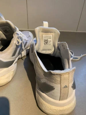 Adidas Crazyflight vita sneakers - Säljer ett par Adidas Crazyflight sneakers i vitt med silverdetaljer och klassiska tre ränder på sidan. Skorna har snörning, mesh på ovansidan för bra ventilation och Jetboost-sula för extra komfort. Perfekta för dig som gillar sportig stil och vill ha något som sticker ut.