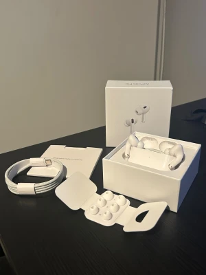 AirPods Pro Gen 2 - Säljer ett par AirPods Pro i nyskick med originalförpackning, extra öronkuddar och laddningskabel. Hörlurarna är trådlösa och erbjuder aktiv brusreducering för bästa ljudupplevelse. Inga synliga defekter eller slitage, allt ser komplett ut.