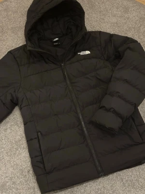 Svart dunjacka från The North Face - Säljer en svart dunjacka från The North Face i strl M med huva och dragkedja i mycket bra skick. Jackan är quiltad och har en clean look med logga på bröstet. Perfekt för kalla dagar och riktigt skön att bära. Passformen är normal och jackan är långärmad. Modellen är 183 och väger 72kg. Enda defekten sitter på baksidan av högerarmen men är lagad snyggt och påverkar inte helheten alls. (Se bild 5-6) Nypris: 2499, mitt pris: 899kr. Kan diskuteras. Hör av dig vid frågor.