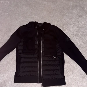 Jätte fräsch och ren Svart cardigan/puffer från Moose Knuckles - Svart cardigan/puffer från jhonells - Moose Knuckles med quiltade paneler, två stora fickor framtill och dragkedja. Jackan har långärmade ärmar, snörning vid kragen och en snygg logotyp på ärmen. Materialet är polyester och dun, perfekt för kyliga dagar. Knappt använd  limited edition jacka från Moose Knuckles , den har varit för stor på mig länge och varit i min garderob jätte bra skick 9/10 🤩🤩🤩 