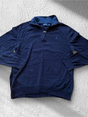 Marinblå half zip tröja Polo Ralph Lauren - Snygg marinblå tröja från Polo Ralph Lauren med half zip och hög krage. Tröjan är långärmad och har ett broderat logomärke på bröstet. Materialet är mjukt och stickat, perfekt för kyliga dagar. Passar dig som gillar klassisk och stilren look.