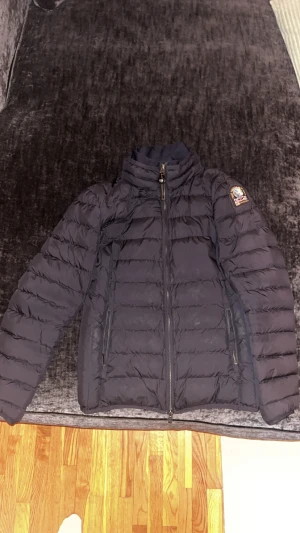 Svart dunjacka från Parajumpers - Säljer en svart dunjacka från Parajumpers med klassisk patch på ärmen och två dragkedjeförsedda fickor framtill. Jackan har quiltad design, hög krage och ljusgrått foder. Perfekt för kalla dagar och riktigt snygg till streetwear.