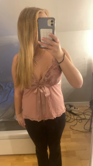 Rosa spetslinnetopp med rosett - Säljer en ljusrosa linnetopp med spetsdetaljer och v-ringad hals. Toppen har en söt rosett framtill och spetskant längs nederkanten. Axelbandslös design med omlott-effekt över bysten. Perfekt för dig som gillar romantisk och feminin stil.