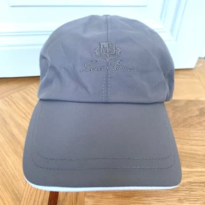 LoroPiana keps grå GRATIS FRAKT - Snygg grå LoroPiana keps med broderad logga framtill. Kepsen är tillverkad i ett slätt, vattenavvisande syntetmaterial och har ett klassiskt sexpanelsutförande. Insidan har ett rutigt foder och etikett med Storm System. Perfekt för dig som gillar stilren och exklusiv look.