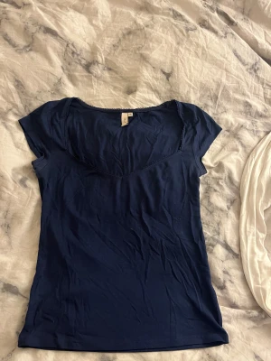 Mörkblå topp med spets från Nelly - Snygg mörkblå topp från Nelly i storlek M. Modellen har korta ärmar och en v-ringad hals med dekorativ spetskant. Tunn och mjuk bomullskvalitet, super skön. Använd 1 gång