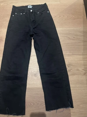 Svarta  jeans från Lager157, XS - Svarta jeans från 157 i storlek XS. Modellen har hög midja, raka ben med wide fit och råa, fransiga benslut för en avslappnad vibe. Klassisk femficksdesign och knappgylf. Perfekta till sneakers eller boots.