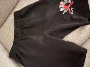 Svarta Jordan x Off-White shorts - Svarta shorts med elastisk midja från Jordan x Off-White. Stort tryck med röd Jumpman och Off-White-logga på ena benet. Sköna och sportiga, perfekta för en streetwear-look.